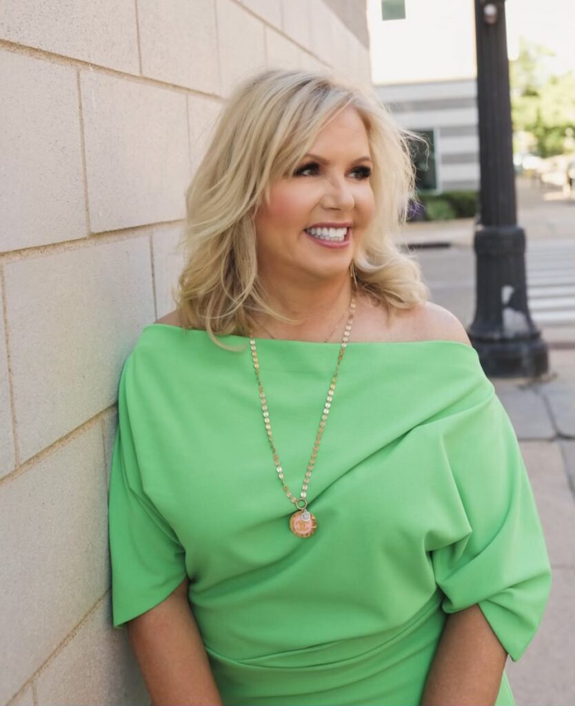 Image of Cyndi Garza in a bright green dress smiling and leaning against a building